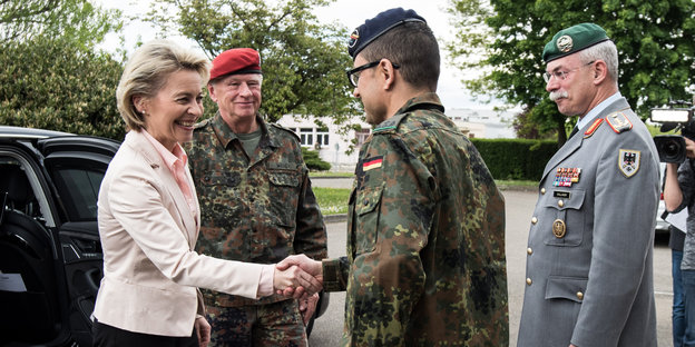 Eine Frau in hellrosa Jacket und drei Männer in Bundeswehruniform begrüßen sich.