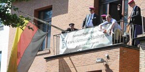 Alberne Männer sitzen mit albernen Mützen und Deutschlandfahne auf einem Balkon