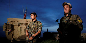 Zwei Soldaten stehen vor einem Panzer mit einer US-Flagge darauf, im Hintergrund ist der Himmel dunkelblau