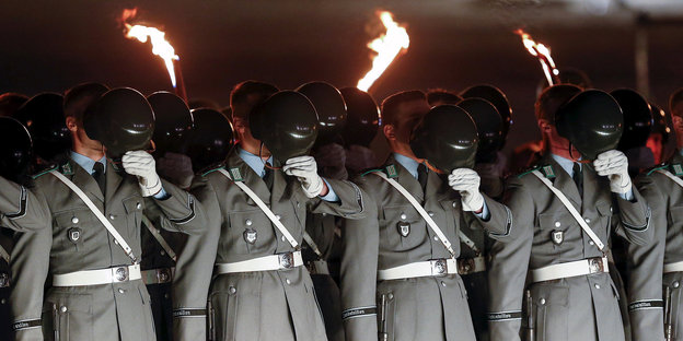 Soldaten mit Fackeln in Reih und Glied halten sich Helme vor das Gesicht