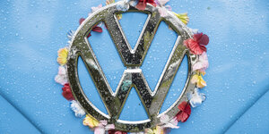 Das Logo eines VW-Autos auf hellblauem Untergrund ist mit Blumenblättern umrundet