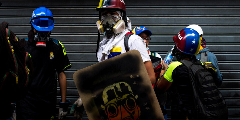 Ein Mann mit bunt angesprühtem Helm und mit Schild in der Hand