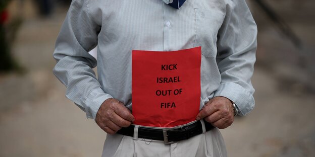 Zu sehen ist der Rumpf eines Manns, der ein Protestschild mit den Worten "Kick Israel out of FIFA" hält