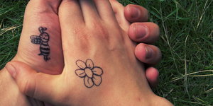 Zwei Hände, auf eine ist eine Biene gemalt, auf die andere eine Blume