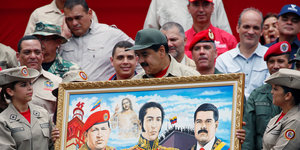 Nicolas Maduro hält ein Ölgemälde in der Hand. Er ist von Menschen in Uniform umringt