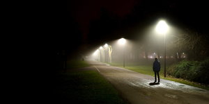 Ein Mensch auf einer von Straßenlaternen beleuchteten, sonst leeren Straße