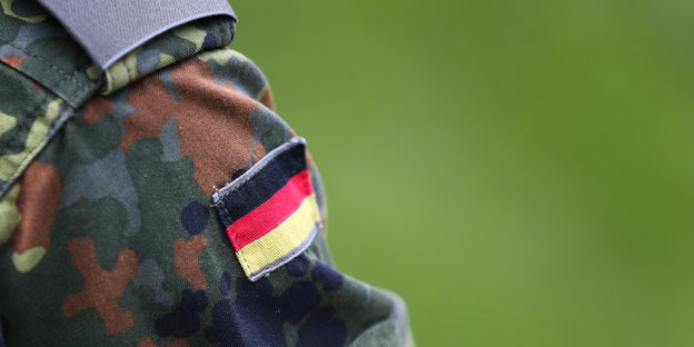 Eine Jacke in Bundeswehrfarben vor Grünem Hintergrund, auf die eine Deutschlandflagge gestickt ist