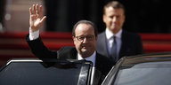 Francois Hollande steht winkend hinter einer Autotür. Unscharf dahinter sieht man Emmanuel Macron