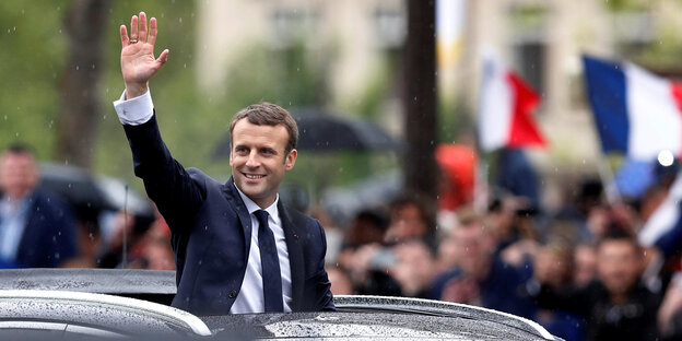 Macron winkt aus dem Schiebedach eines Autos heraus