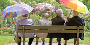 Seniorinnen sitzen auf einer Bank und halten bunte Regenschirme in den Händen