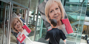 Menschen tragen Plakate mit dem Konterfei Hannelore Krafts durch eine Tür