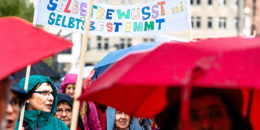 Frauen tragen Kapuzen und Regenschirme sowie ein Transparent mit den Worten "Selbstbewusst und selbtsbestimmt" durch die Hamburger Innenstadt.