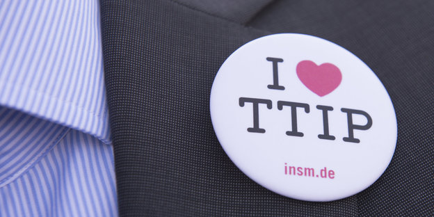 An einem Anzugrevers hängt ein Anstecker, auf dem „Ich <3 TTIP“ steht