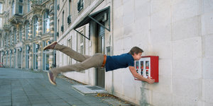 Ein Mann steht waagrecht von einem Kaugummiautomaten ab, der an der Wand befestigt ist. Er scheint also in der Luft zu schweben.