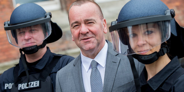 Niedersachsens Innenminister Pistorius steht zwischen zwei behelmten Polizist_innen