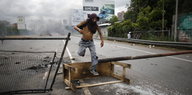 Ein Mann mit vermummtem Gesicht springt über eine Straßensperre in Caracas