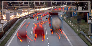 rote Rücklichter von zwei Autos und einem Lkw auf einer Autobahn erschwimmen
