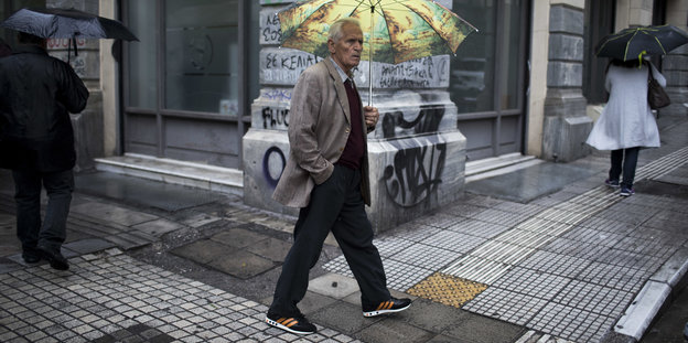Ein griechischer Rentner äuft bei Regen auf der Straße