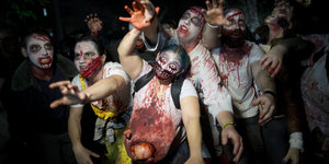 Eine Gruppe Menschen hat sich als blutverschmierte Zombies verkleidet und reckt die Arme in die Gegend