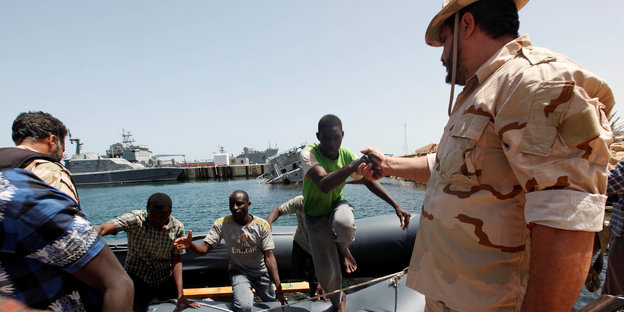 Ein libyscher Soldat reicht einem Flüchtling, der aus einem Boot steigt, die Hand