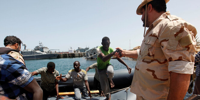 Ein libyscher Soldat reicht einem Flüchtling, der aus einem Boot steigt, die Hand