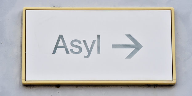 Auf einem Schild an einer Wand steht „Asyl“ mit einem Pfeil