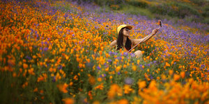 Eine Frau sitzt in einem Blumenfeld und macht mit Hilfe eines Handy-Sticks ein Foto von sich