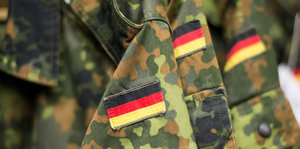 Drei Deutschlandflaggen sind auf drei Ärmel von Tarnkleidung genäht