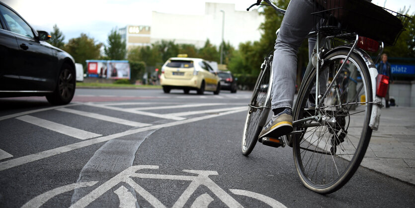 Eine Person auf einem Fahrrad bieg auf einem Radstreifen in einen Kreisverkehr ein, neben ihr fahren Autos