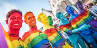 Männer sind mit Regenbogenfahnen bemalt und lachen in die Kamera