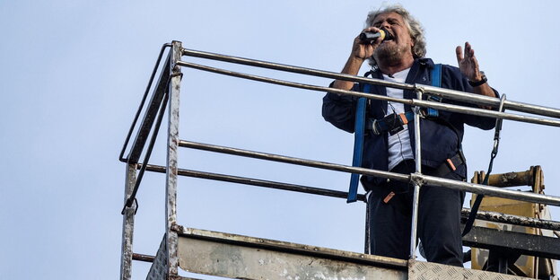 Beppe Grillo schreit in ein Mikrofon, während er auf einem Kran steht