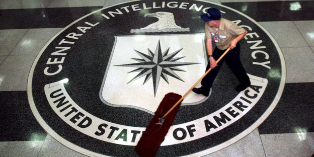 Ein Putzmann reinigt einen Boden in den das Emblem der CIA eingelassen ist