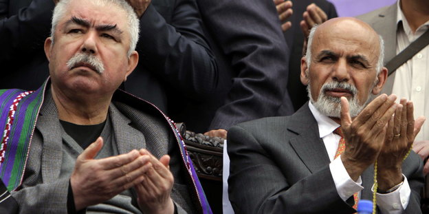 Raschid Dostum und Aschraf Ghani sitzen nebeneinander und haben die Hände zum Gebet erhoben