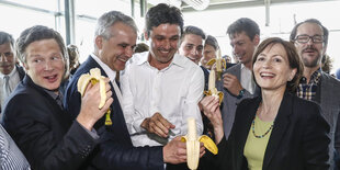 Menschen mit glücklichem Gesichtsausdruck stehen beieinander und essen Bananen