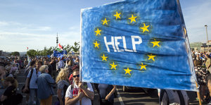 Demonstrierende mit einem Plakat, auf dem inmitten der europäischen Flagge "Help" steht