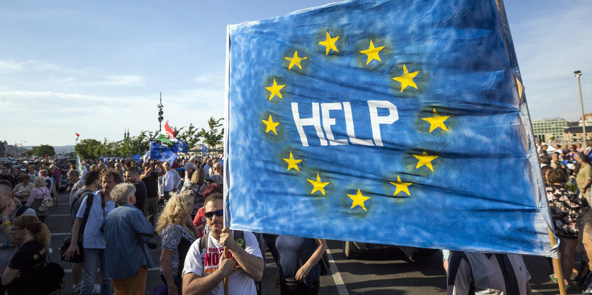 Demonstrierende mit einem Plakat, auf dem inmitten der europäischen Flagge "Help" steht