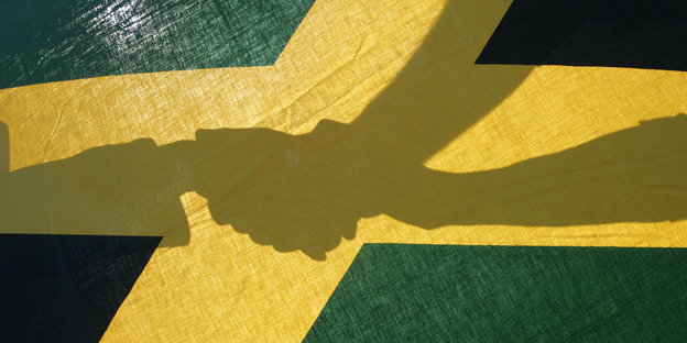 Schatten von Händen dreier Menschen auf einer Jamaika-Fahne