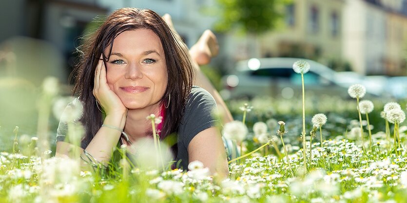 Eine Frau liegt auf einer Grünflache, Pusteblumen umgeben sie