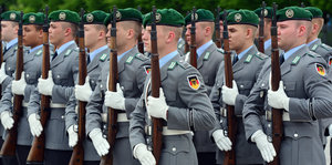 Soldaten in grauen Uniformjacken und mit grünen Barretts stehen mit erhobenen Waffen in Reih und Glied