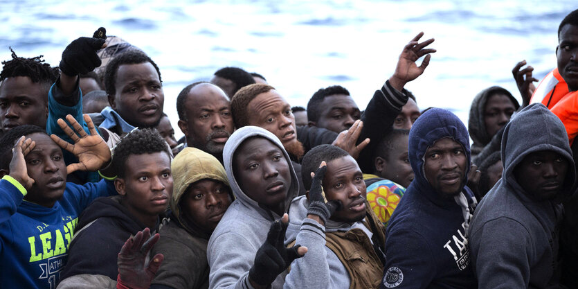 Viele Männer sitzen in einem Boot, einige heben die Hand