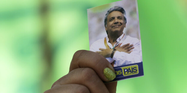 Eine Hand hält ein Bild mit Wahlwerbung für den Präsidenten Lenín Moreno vor grünem Hintergrund