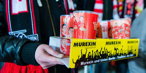 Ein Fan des Fussballclub Union Berlin mit vier Mehrwegbechern in seinen Händen