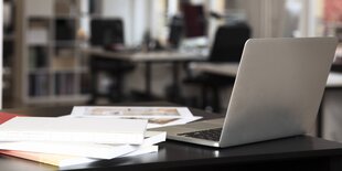 Ein Laptop und ein Stapel Bücher auf einem Schreibtisch in einem Büroraum