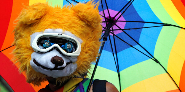 Ein Mensch mit Regenbogenschirm und Teddybärenmaske