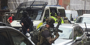 Bewaffnete Polizisten drängen sich zwischen parkenden Autos