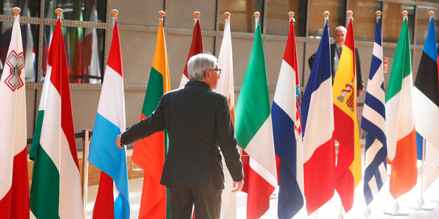 Jean-Claude Jucker geht an den Flaggen verschiedener Länder im EU-Hauptquartier entlang