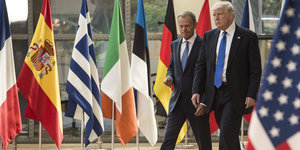 Zwei Männer in Anzügen gehen nebeneinander, um sie herum sind verschiedene Nationalflaggen aufgestellt