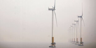 Im Nebel stehende Windräder an der Küste