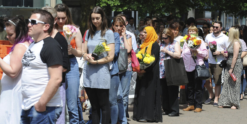 Menschen stehen in einer langen Schlange, sie halten Blumen in ihren Händen