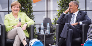 Angela Merkel und Barack Obama sitzen auf einer Bühne nebeneinander und lachen